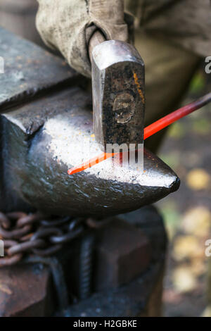 Blacksmith forges red hot steel rod on anvil in outdoor rural smithy Stock Photo