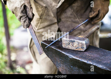 Blacksmith processing steel rod by file on anvil in outdoor rural smithy Stock Photo