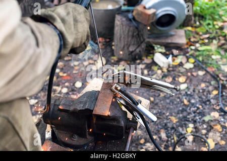 Welder welds iron ring by point electric welding in outdoor rural workshop Stock Photo