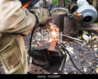 Welder welds steel buckle by spot electric welding in outdoor rural workshop Stock Photo