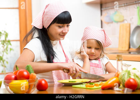 Mother teaching child making salad in kitchen. Mom and kid chopping vegetable on cutting board with knife. Cooking concept of ha Stock Photo