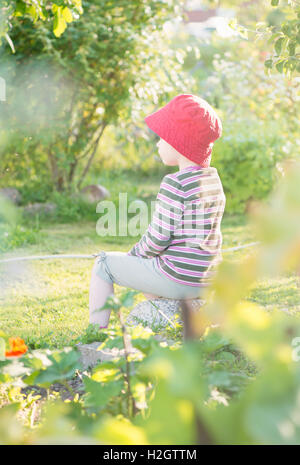 Tranquil summer scene, young girl sitting in garden, watching plants and flowers, Sweden Stock Photo