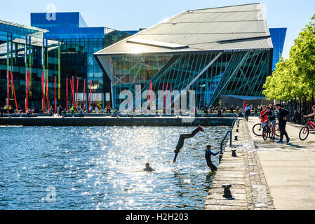 Boys jump into water at Hanover Quay on Dublin’s Grand Canal with Bord Gáis Energy Theatre behind Stock Photo