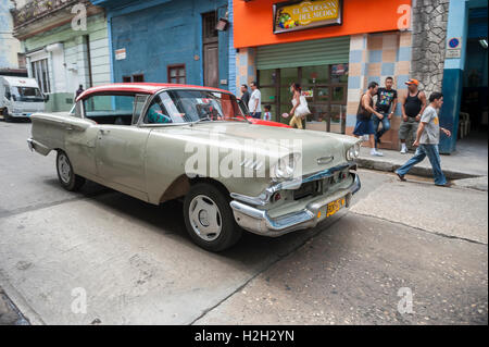 HAVANA - JUNE 15, 2011: Cubans talk on the corner as a vintage American car serving as taxi drives past in Central Havana. Stock Photo