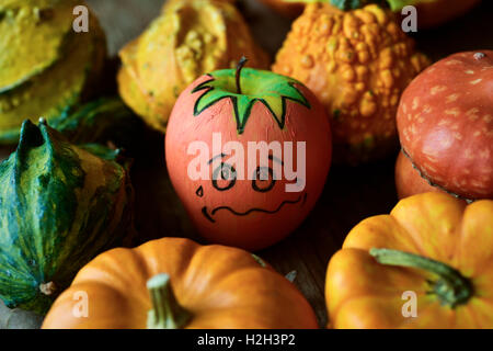 an apple disguised as a pumpkin with a funny face trying to go unnoticed between different real pumpkins Stock Photo
