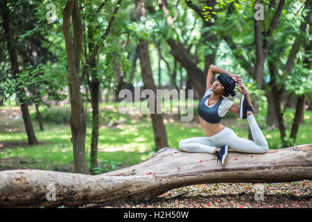 Young woman doing yoga poses on a tree trunk in a park in India. Stock Photo