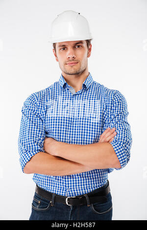 Serious handsome young man architect in building helmet standing with arms crossed over white background Stock Photo
