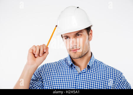 Thoughtful young man builder in building helmet with pencil thinking Stock Photo