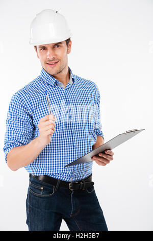 Serious young man builder in hard hat writing on clipboard Stock Photo