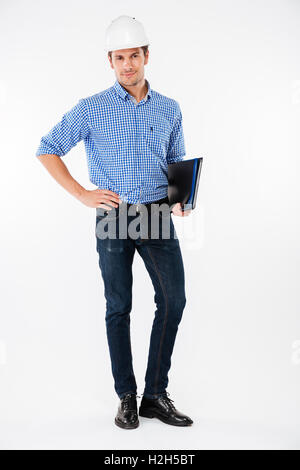 Confident young man builder in hard hat standing and holding folder Stock Photo