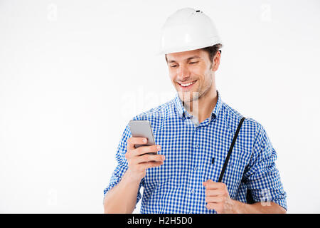 Smiling young man builder in hard hat using mobile phone Stock Photo