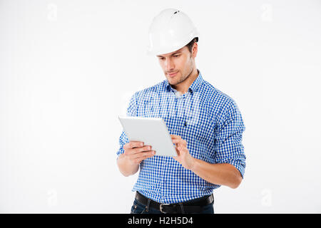 Serious young man architect in hard hat standing and using tablet Stock Photo