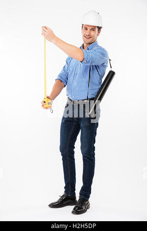 Full length of smiling young man architect in hard hat standing and using measuring tape Stock Photo