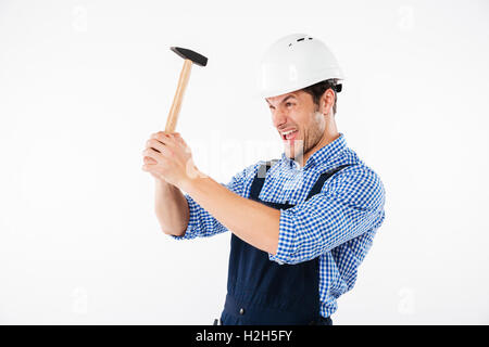 Funny young builder applying hummer to his head in helmet and having fun isolated on a white background Stock Photo
