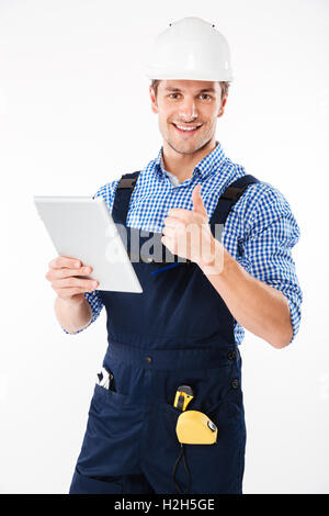 Happy male builder showing thumb up and holding pc tablet isolated on a white background Stock Photo