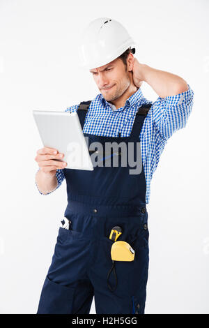 Thoughtful confused builder in helmet scratching his head and holding pc tablet isolated on a white background Stock Photo