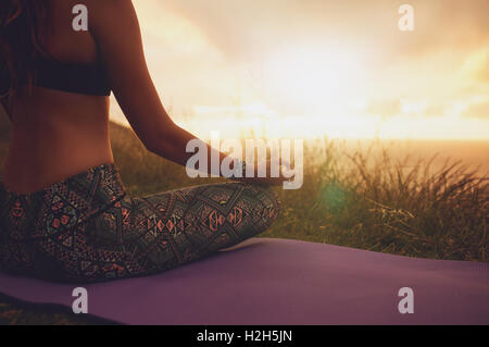 Close up shot of female sitting in lotus yoga pose on exercise mat, with focus on hands. fitness female meditating outdoors duri Stock Photo