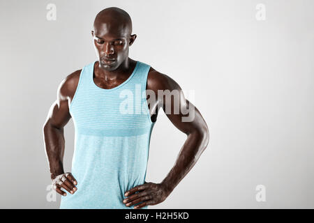 Portrait of masculine young african man with shaved head and hands on hips over grey background. Muscular black male model looki Stock Photo