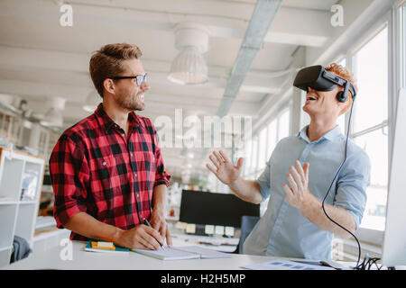Young man testing virtual reality technology with colleague in office. Colleagues working on improving VR headset technology exp Stock Photo
