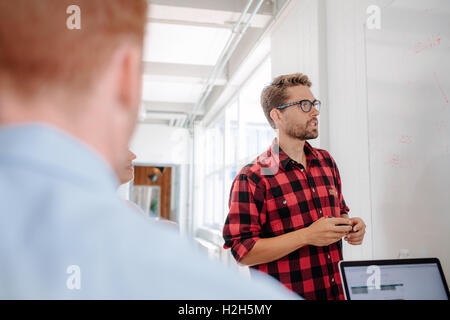 Businessman in casuals giving presentation on white board to colleagues in conference room. Stock Photo