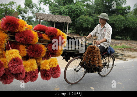 Man wearing a North Vietnamese Pith Helmet and transporting feather dusters on a bicycle in North Vietnam Stock Photo