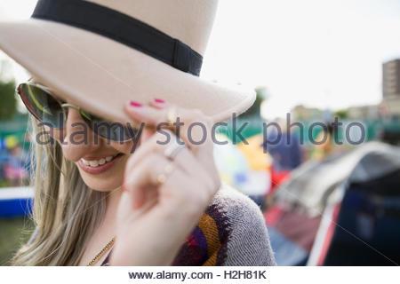 Close up portrait young woman wearing hat and sunglasses looking down at summer music festival campsite