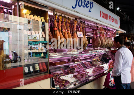 Butcher with typical Iberian hams  in  a big market in central Barcelona. Spain Stock Photo