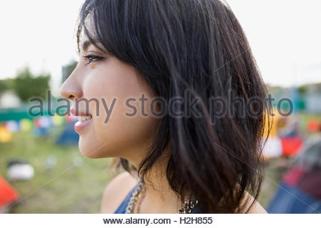 Close up profile portrait smiling young woman with black hair looking away at summer music festival campsite