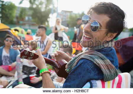 Portrait enthusiastic young man playing ukulele at summer music festival campsite