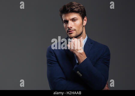 Thoughtful young brunette man in blue jacket thinking about something isolated on a gray background Stock Photo