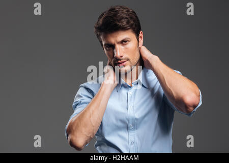 Confident young businessman in blue shirt touching his neck on gray background Stock Photo