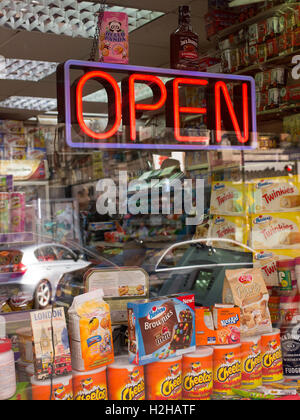 Shop window of a convenience store with open sign in neon lights. Various products and sweets on sale below. Stock Photo