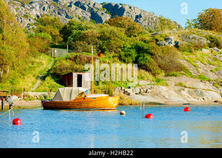 Old wooden motorboat with sailing mast moored in seaside bay close to cliffs and shrubbery. Stock Photo