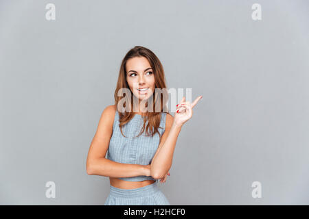 Cheerful lovely young woman standing and pointing away over grey background Stock Photo