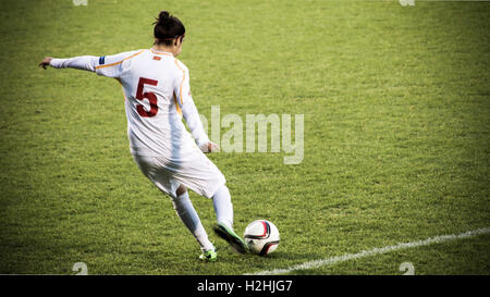 Female footballer kicking ball mid-game Stock Photo
