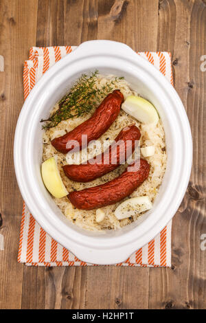 fresh sauerkraut with smoked sausages, onions, garlic, crushed peppercorn and thyme in a white slow cooker Stock Photo