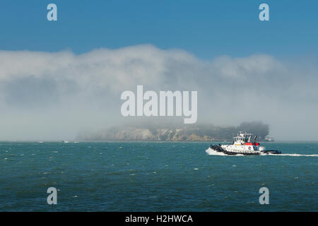 Crowley Maritime Tugboat Veteran Passes Alcatraz As Sea Fog Rolls Over The Island. Stock Photo