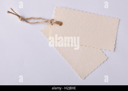 Two beige textured paper tags with string tied on white background. Top view Stock Photo