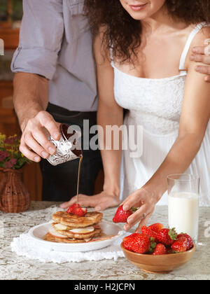 Young couple making a plate of pancakes with strawberries an apples together in the kitchen Stock Photo