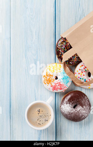 Colorful donuts in paper bag and coffee cup on wooden table. Top view with copy space Stock Photo