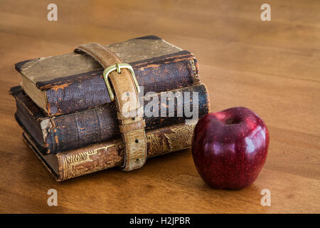 Three old school books wrapped with an old belt with one red apple for the teacher abstract on wood, USA, vintage objects still life, antique images Stock Photo