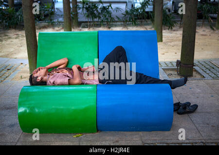 A young Malaysian man takes a nap on a park bench in Kuala Lumpur, Malaysia, Southeast Asia. Stock Photo
