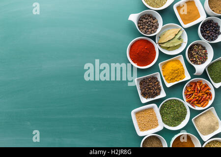 Various dried herbs and spices in bowl on green chalkboard. Stock Photo