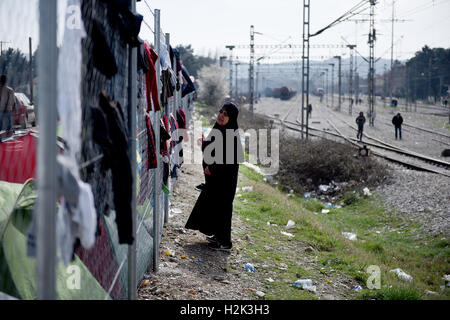 A refugee woman hangs clothes from a fence, next to the railway lines, in a refugee camp, at the northern Greek village of Idomeni. Thousands of refugees and migrants were stranded for months at the Greek Macedonian border, at the refugee camp near the village of Idomeni, until the Greek government decided to evacuate the area. Stock Photo