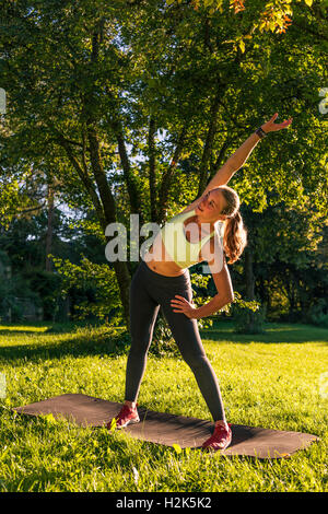 Warmup exercise, young woman in sportswear doing workout on mat in park, Munich, Upper Bavaria, Bavaria, Germany Stock Photo