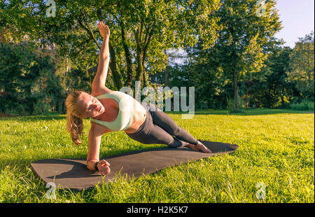 Young woman in sportswear doing side plank, workout on mat in park, Munich, Upper Bavaria, Bavaria, Germany Stock Photo