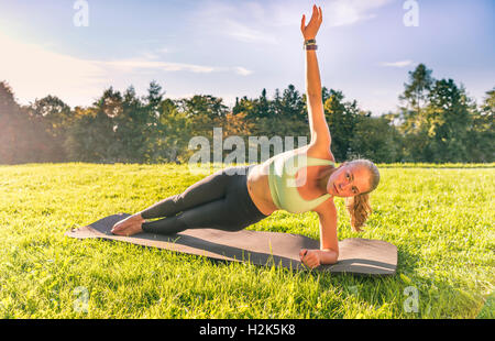 Young woman in sportswear doing side plank, workout on mat in park, Munich, Upper Bavaria, Bavaria, Germany Stock Photo
