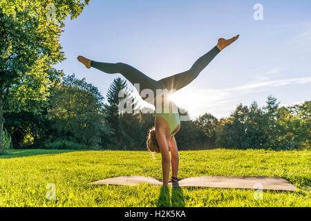 Handstand, young woman in sportswear doing workout on mat in park, Munich, Upper Bavaria, Bavaria, Germany Stock Photo