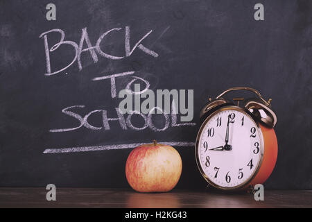 Alarm clock and an apple against a blackboard Vintage Retro Filter. Stock Photo