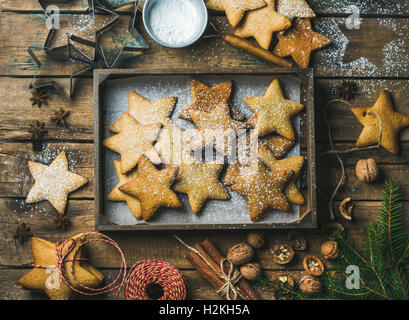 Gingerbread star shaped cookies in wooden tray with baking paper at bottom, sugar powder, nuts, spices, baking molds, fir-tree b Stock Photo
